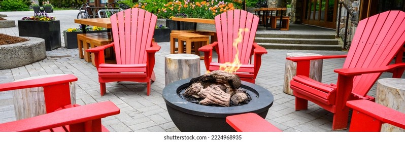 Bright red Adirondack chairs around a gas fire pit, seating in an outdoor gathering place
				