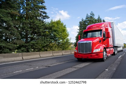 Bright Red Bonnet American Modern Long Haul Big Rig Semi Truck With Dry Van Semi Trailer Transporting Commercial Cargo Moving On The Wide Multiline Green Highway Road 