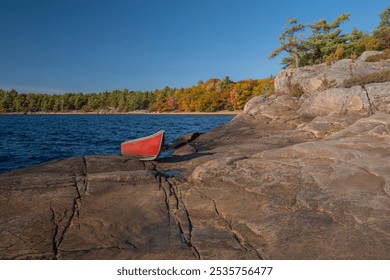 A bright red canoe on the rugged rocky shore of a lake with colorful fall trees in the background. Killbear Provincial Park, Ontario, Canada. - Powered by Shutterstock