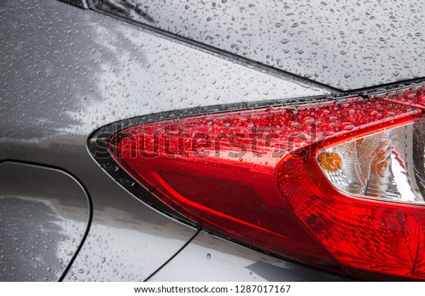 Bright red car back light covered with\
rain drops and neutral grey polished car\
body