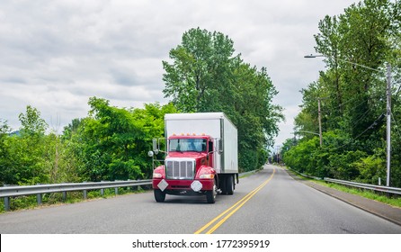 Bright Red Day Cab Big Rig Semi Truck For Local Delivery  And Business Freights With Long Box Trailer Transporting Commercial Cargo Driving On The Green City Street With Frees And Dividing Lines