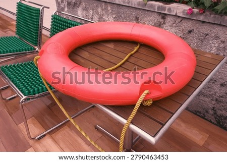 Bright red donut pool float resting on patterned tiles by a luxurious swimming pool, ready for summer relaxation.