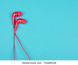 Bright red earbud headphones isolated on a bright blue background with copy space on the right for your text (minimal concept, top view)