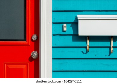 A bright red exterior door with a glass window, metal door knob and lock. The colorful teal blue horizontal wooden clapboard residential wall has a small white doorbell button and white letterbox.  - Powered by Shutterstock