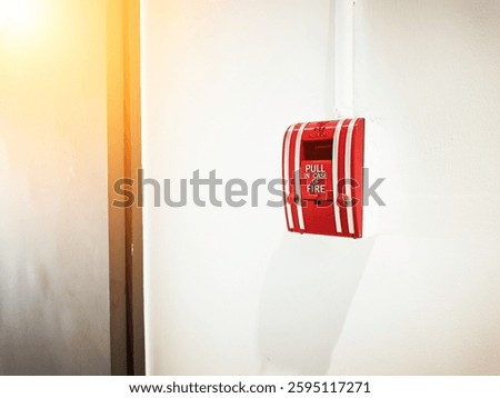 A bright red fire alarm pull station is mounted on a white wall, illuminated by natural light. It serves as an essential safety device for emergencies.