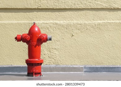 Bright red fire hydrant on concrete sidewalk against textured yellow wall, safety equipment, emergency urban utility