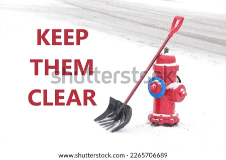 Bright red fire hydrant in the snow with a shovel. KEEP THEM CLEAR  message or words written beside the hydrant.