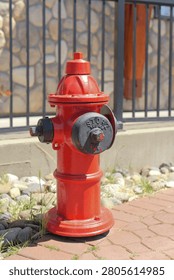 Bright red fire hydrant standing proudly on a brick walkway beside a stone wall