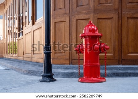 A bright red fire hydrant stands next to wooden building, showcasing urban safety