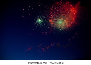 Bright red fireworks with sparks and smoke, small green fireworks explode in them. High quality photo