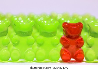 A bright red generic gummy bear in line with green gummy bears. Odd one out concept or one wrong person. Shallow depth of field. - Shutterstock ID 2254824097
