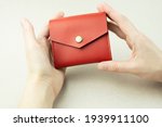 bright red leather wallet in female hands close-up on a gray background