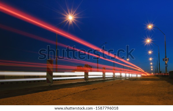Bright red lines of city traffic on a bridge\
with the lanterns. Highway road with car light speed trails. View\
of the evening city at dusk against the blue sky. Shot from a low\
point at asphalt.
