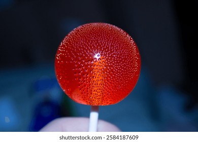 A bright red lollipop with tiny bubbles inside on a dark background. High quality photo