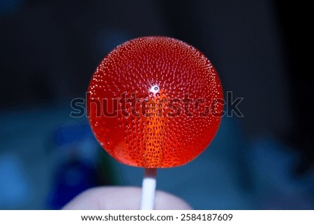 A bright red lollipop with tiny bubbles inside on a dark background. High quality photo