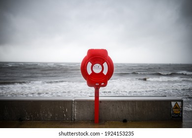 Bright Red Modern Lifebuoy Warning On Storm Sky Ocean Coastline. Life Saving Equipment Preserver Emergency Station To Help Prevent Drowning In Sea