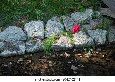 The Bright Red Paper Plane Is Lying On The Rocks On The River Bank. The Loneliness And Crash Concept 