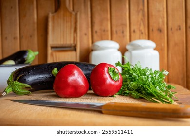 Bright red peppers and eggplant rest on a wooden cutting board alongside fresh parsley and a kitchen knife. A rustic backdrop adds warmth to this culinary setting. - Powered by Shutterstock