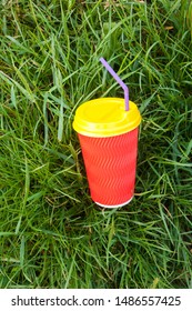 Bright Red Plastic Cup With Yellow Lid And Purple Bendy Drinking Straw (tube) In The Grass.