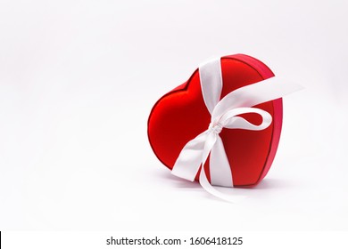 Bright red satin box in the shape of a heart, tied with a white ribbon with a bow on a white background. Concept of love, Valentine's day, gift, beloved, surprise, present, feelings. Copy space