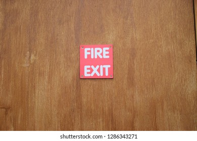 Bright red square fire exit sign nailed to a wooden background 