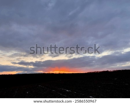 Bright red sunset. Cloudy sky. Winter evening. Field under snow. Sun sets over the horizon.