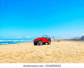 a bright red Suzuki Jimny (or similar model) is parked on a sandy beach with a clear blue sky. Waves crash on the shore in the background.