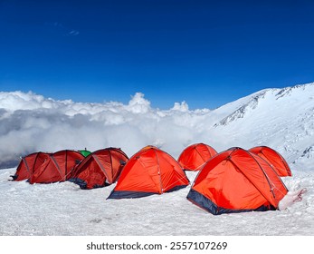 Bright red tents on a snowy mountain slope above the clouds, surrounded by majestic peaks and a deep blue sky, capturing the essence of high-altitude camping, adventure, and breathtaking landscapes.  - Powered by Shutterstock