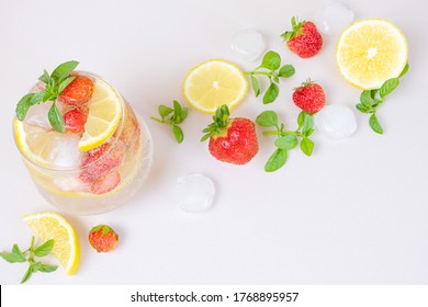 Bright refreshing drink for the summer, cold strawberry lemonade juice in a glass with ice cubes, top view. Around - slices of lemon, strawberries, mint leaves, ice. Flat lay.