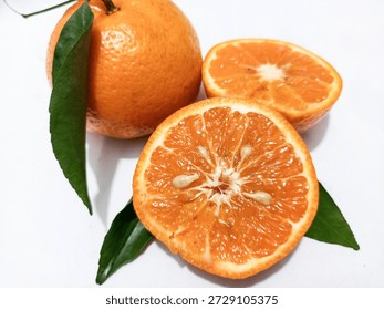 A bright and refreshing high-angle shot featuring fresh organic mandarin oranges against a clean white background. The composition includes one whole orange with a vibrant green leaf still attached to the stem, alongside a mandarin cut in half to reveal its juicy, segmented interior and seeds. The fruit's skin displays a rich, pebbled orange texture, and the internal sections are glistening, highlighting their freshness and high juice content. The natural lighting emphasizes the vivid colors and organic quality of the citrus. This high-resolution image is ideal for health and nutrition topics, culinary blogs, juice packaging, and healthy lifestyle branding. Its minimalist aesthetic and clear focus make it a versatile asset for food-related advertisements and educational materials about vitamin C and citrus fruits.