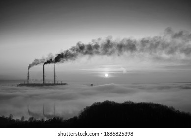 Bright rising sun at thermoelectric power plant. Thermal chimneys producing dense smoke with toxic gases into atmosphere. Concept of ecology and environmental pollution. Black and white image