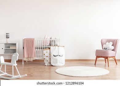 Bright scandinavian baby room with rocking horse, white nursery and pink armchairs, posters on the wall