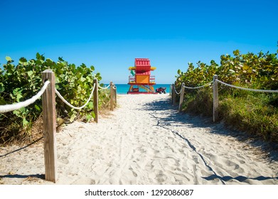 Bright Scenic View Of Classic Sand Dune Path Lined With Tropical Greenery Leading To The Vibrant Blue Sea With Lifeguard Tower On South Beach, Miami, Florida, USA