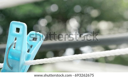 Bright shot of close-up blue clothespin hung freely on white clothesline rope with blurred house roof and many bokehs from trees as background