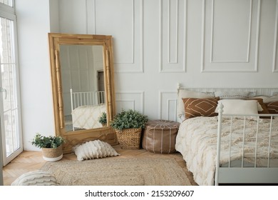 Bright and spacious bedroom with a white wall, an eco-wooden mirror and flower pots. Cozy bright rustic style bedroom, boho style bedroom. - Powered by Shutterstock