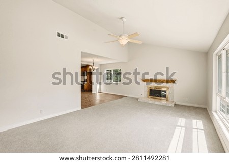 Bright and spacious empty living room interior featuring vaulted ceilings, light gray carpet, a marble fireplace, a ceiling fan, and large windows bri