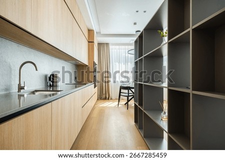Bright and spacious kitchen features sleek wooden cabinets and open shelving. Natural light filters through large windows, creating a warm atmosphere in this urban apartment setting