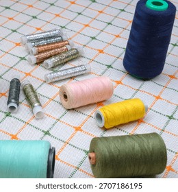 bright spools of sewing threads of various colors and gold silver wire, neatly arranged on the surface of a white green checkered tablecloth, ready for use in sewing and embroidery