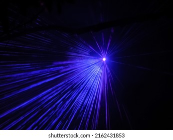A bright spotlight projects neon blue beams in a dark night space. Laser show.