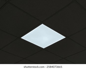 A bright square LED panel embedded in a dark, speckled acoustic ceiling, contrasting with the surrounding tiles.
