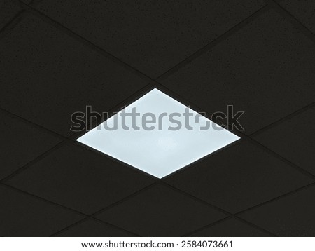 A bright square LED panel embedded in a dark, speckled acoustic ceiling, contrasting with the surrounding tiles.