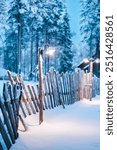 Bright Street Light Illuminating the Snow Covered Walking Path and Wooden Fence in the Forest on a Dark Winter Evening