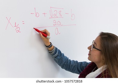 Bright student solving math equation. Blonde young girl writing with red pen on white board. Intelligent woman concept, teacher explaining problem