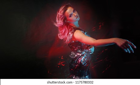 Bright and stylish young woman dancing in club, color light, motion effects. Black background, long exposure