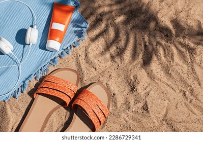 Bright summer beach vacation or travel lifestyle concept flat lay with suncream, headphones and a flip flops on the sand. Top view - Powered by Shutterstock