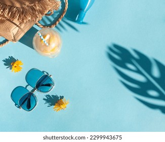 Bright summer beach vacation or travel lifestyle concept frame with lemonade, a straw bag, sunglasses and sunscreen spray. Top view. Copy space