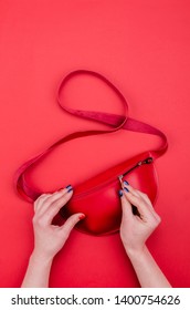 Bright Summer Fashion Ladies Accessories. Stylish Red Leather Handbag Or Fanny Pack On A Red Background. Women Hands With Bright Manicure Open Bag. Top View. Flat Lay. Copy Space. Mock Up