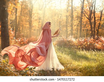bright summer photo of mysterious beauty in morning forest, lady in shiny white dress and peach pink cloak with long train and hood, back to camera and turned face, girl with dark hair and barn owl