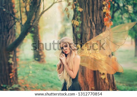 bright summer photo mysterious forest fairy fell in love with prince, girl with puppet happy face, blond long hair and blue eyes, lady angel in green dress peeps modestly interest. Yellow trees. 