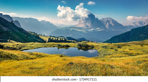 Bright summer view of small pond and Sassolungo (Langkofel) range on background in National Park Dolomites, South Tyrol, Italy, Europe. Blooming yollow flowers on the slope of Gardena valley.
